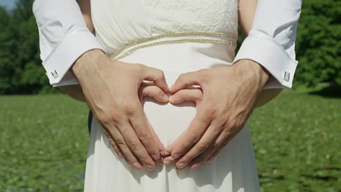 特写: 无法识别的夫妻用手在怀孕的腹部上使爱心