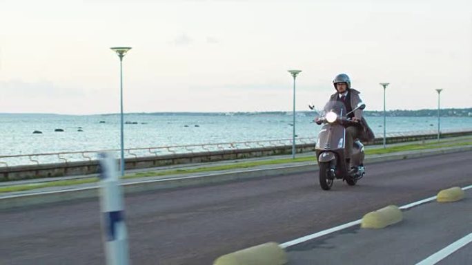 穿着优雅的米色风衣的年轻人在海边的路上骑着一辆复古的踏板车。