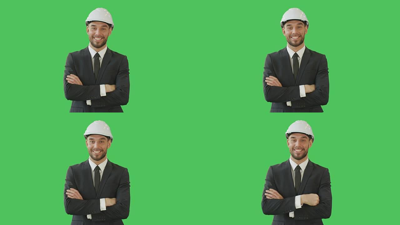 英俊的微笑商人穿着量身定制的西装，双臂交叉着安全帽。背景是绿屏模型。