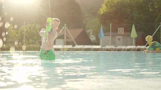 慢动作: 快乐男孩在美丽的夏日日落时阳光明媚的假期在游泳池里玩水枪