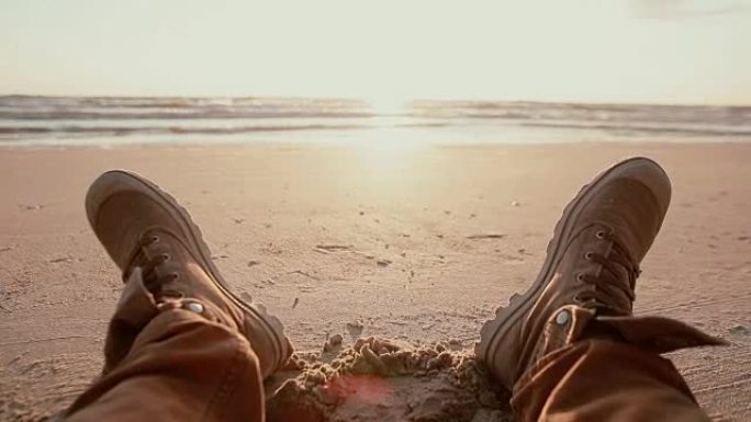 黎明时分，穿着棕色靴子的2英尺在沙滩上休息