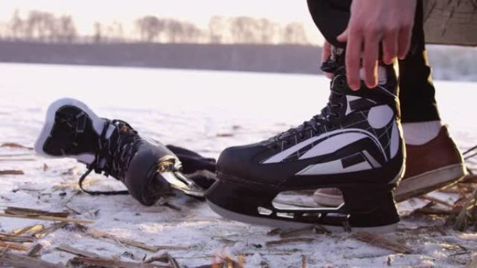 4k十几岁的男孩在冰冻的湖上系着溜冰鞋鞋带，慢动作
