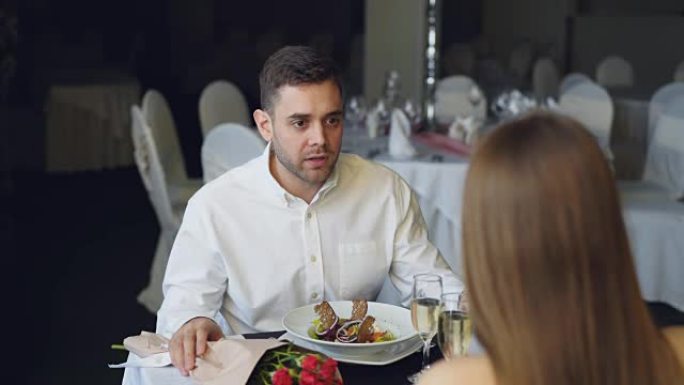 年轻夫妇在餐厅用餐时吵架，大喊大叫。可以看到一束玫瑰花，火花香槟酒杯和装有食物的盘子。