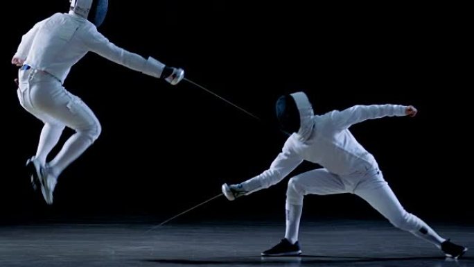 两名专业击剑手在花剑搏斗中表现出精湛的剑术。他们躲闪，跳跃，推力和弓步。拍摄孤立在黑色背景和慢动作中