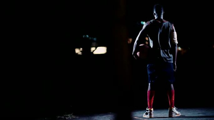 篮球运动员在夜间将篮球放在臀部