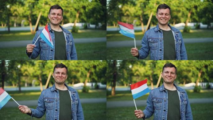 快乐的家伙快乐的游客挥舞着荷兰国旗，微笑着看着相机的慢动作肖像。民族自豪感、来访国家和人民观念。