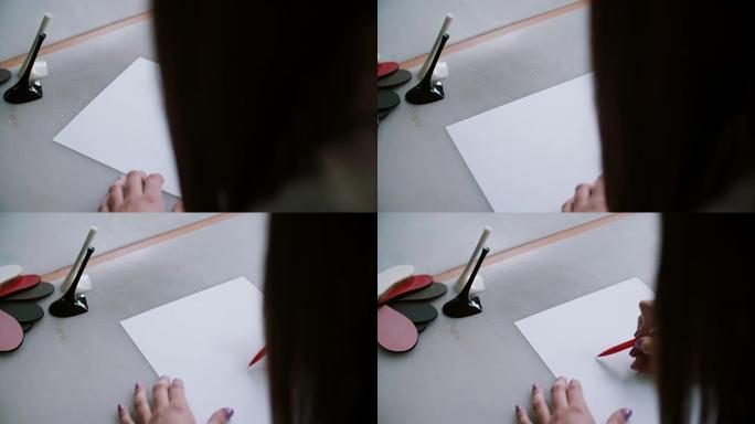 女人坐在桌子上，脚后跟和纺织品样品，在纸上素描。向左滑动。4K