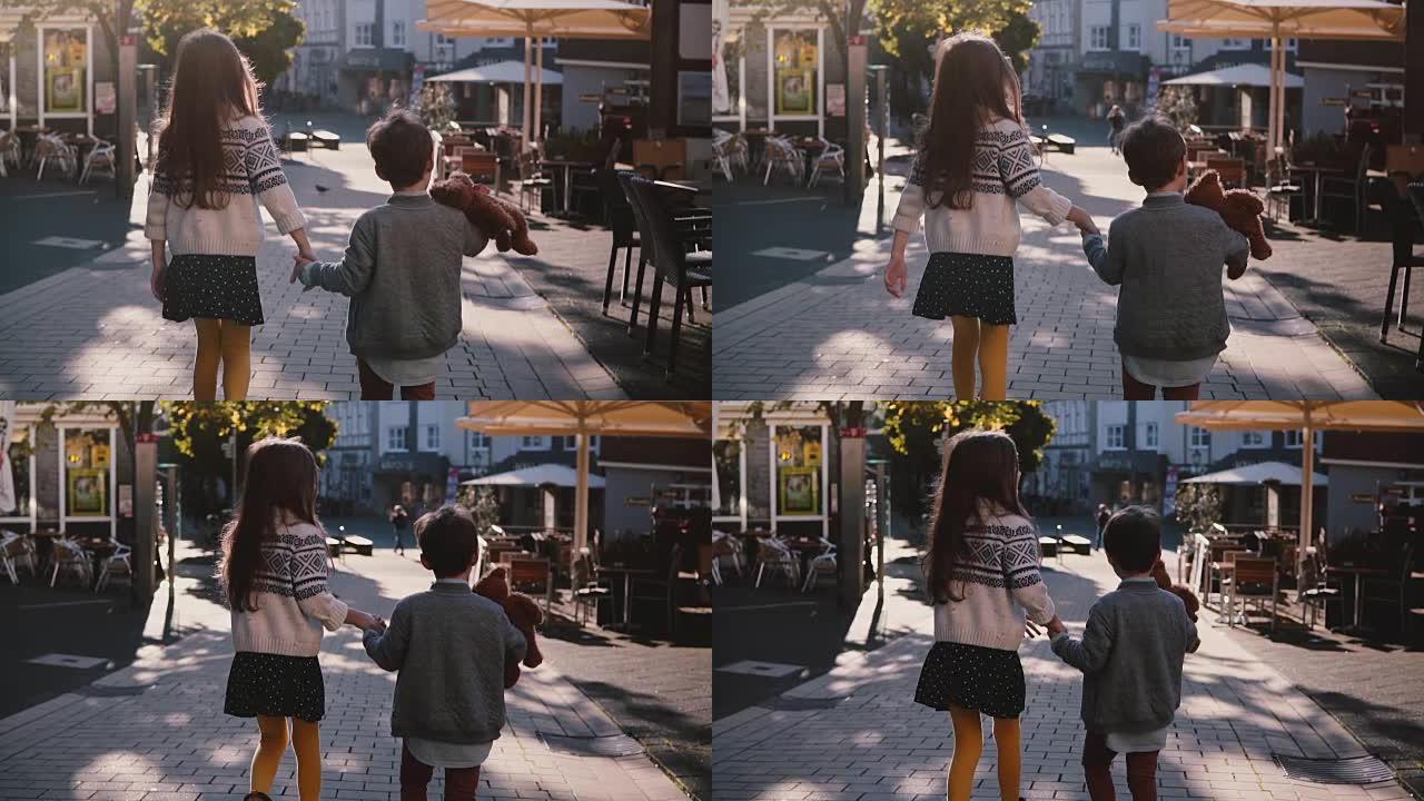 两个孩子一起散步，牵着手。慢动作。后视图。小孩子在阳光明媚的日子里探索老城区的街道