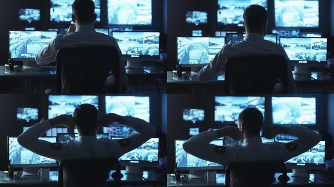 安全官员在充满显示屏的黑暗监控室里的计算机上工作时正在喝咖啡。