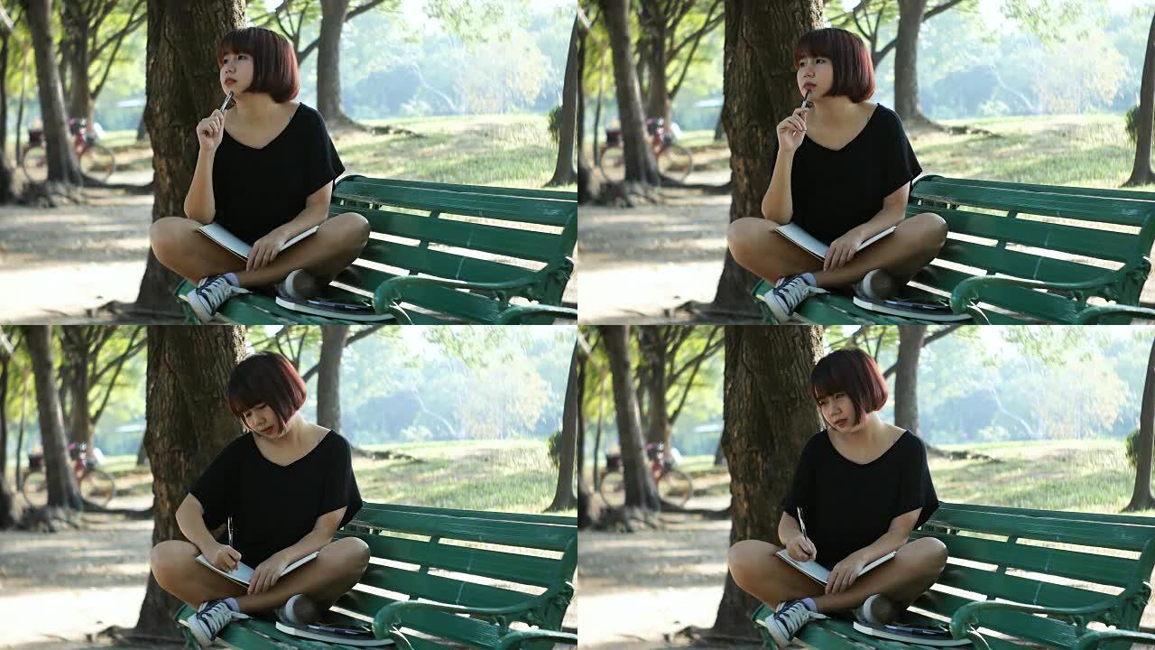 快乐的潮人年轻的亚洲女人在公园写日记。快乐的潮人年轻亚洲妇女在公园做笔记本。学生在户外学习。生活方式