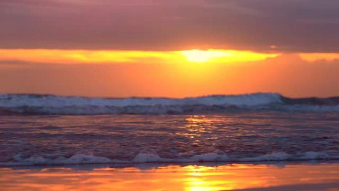 特写: 荡漾的海浪在巴厘岛引人注目的粉红色日落时冲刷沙滩