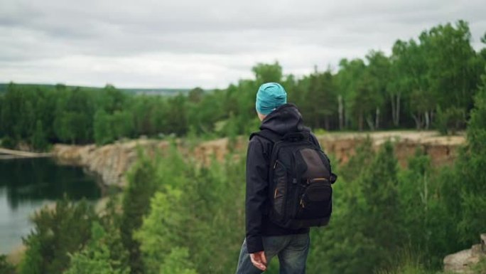 带背包的年轻人游客的慢动作肖像下山，在悬崖山湖和树林下观看激动人心的景色。