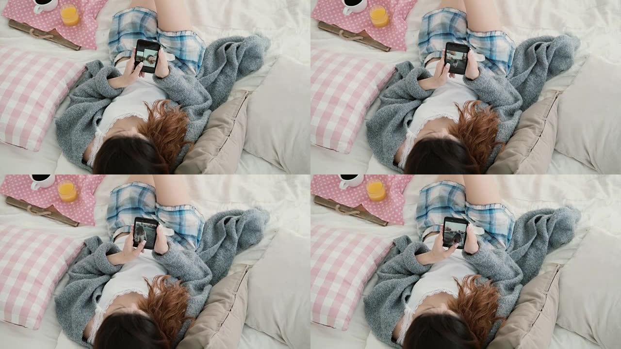 年轻漂亮的女人躺在床上，拿着手机。女孩在智能手机上观看旅行中的照片