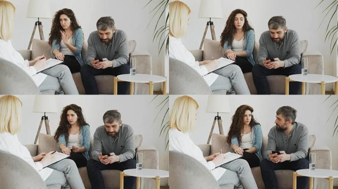 女性专业心理学家在室内办公室访问期间，年轻女子争吵和男友在智能手机上冲浪时，听和写笔记心理治疗
