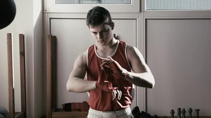 年轻的拳击手在手上拉着红色绷带，并摆出战斗姿势。