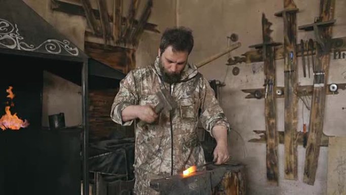 大胡子的年轻人铁匠用火花烟花在铁砧上手工锻造铁铁刀