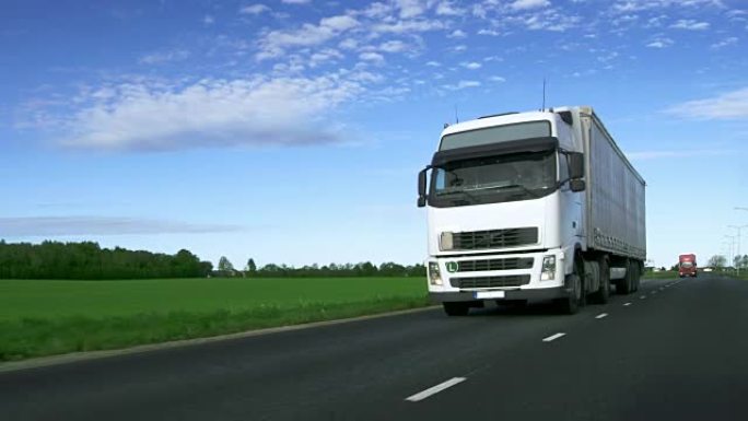 带货运拖车的超速白色半卡车在高速公路上行驶，路边有田野。