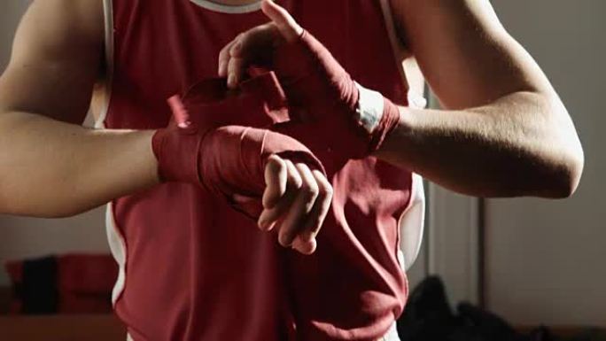 年轻的拳击手在手上拉着红色绷带，并摆出战斗姿势。