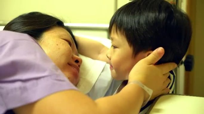 亚洲妇女躺在医院病床上的昏迷，她的儿子坐在她旁边