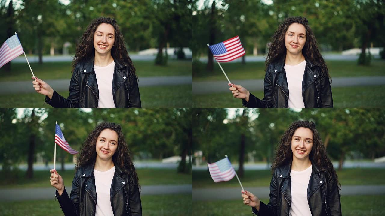 慢动作肖像快乐的美国游客挥舞着美国国旗，看着相机和微笑。世界旅游，参观国家和人民的观念。