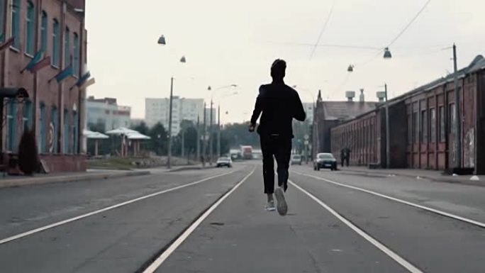 一个男人在一条老街的中间跑得很快。实时拍摄。自由。镜头跟随运动员穿梭于电车轨道之间