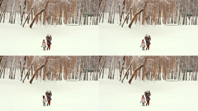 年轻的母亲和她的孩子站在白雪皑皑的公园里
