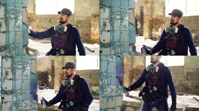 严肃的大胡子家伙专注于用气溶胶涂料在废弃建筑内的旧肮脏柱子上画涂鸦。男人穿着便服和手套。