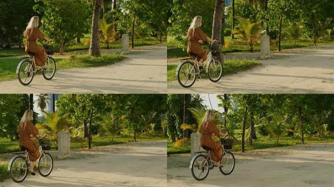 穿着连衣裙的美女骑着自行车在路上穿过正宗的村庄。南亚自然，风景秀丽的森林在路边生长。