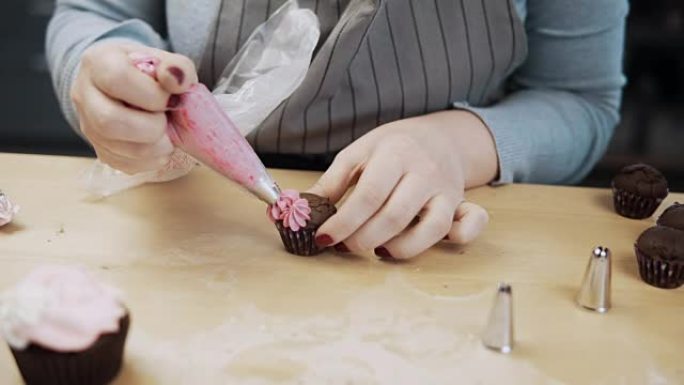 使用糕点袋，用粉红色奶油装饰巧克力蛋糕的女性手的特写视图