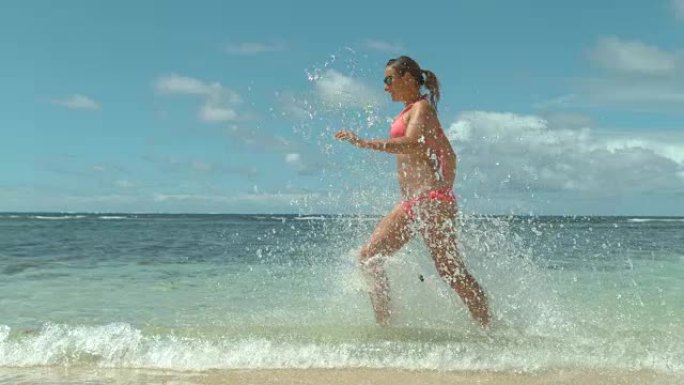 慢动作: 顽皮的年轻白人妇女穿着粉红色泳衣在海水中奔跑