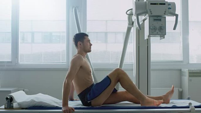 在医院，该男子坐在床上等待x光机扫描腿部受伤的侧视图。扫描骨折、四肢骨折、癌症或肿瘤。拥有技术先进的