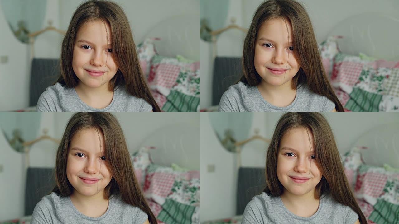 可爱的小女孩在家里的卧室里看着相机和蔼地微笑的特写肖像