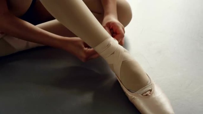 特写镜头，女孩的脚穿着芭蕾舞拖鞋和手试图穿上鞋子，并在腿上系上缎带。足尖鞋、舞蹈和服装概念。