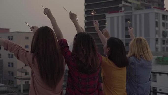 屋顶派对上年轻人的户外镜头。快乐的亚洲女孩朋友群在傍晚日落时在屋顶派对上享受和玩烟火。节日庆祝节日派