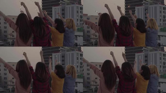 屋顶派对上年轻人的户外镜头。快乐的亚洲女孩朋友群在傍晚日落时在屋顶派对上享受和玩烟火。节日庆祝节日派