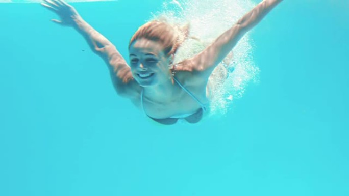 迷人的女人在游泳池里潜水