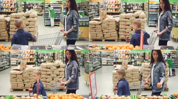 年轻的女士和她的儿子穿着牛仔夹克一起购物，他们正穿过超市的过道环顾四周，抚摸着水果。商店和人的概念。