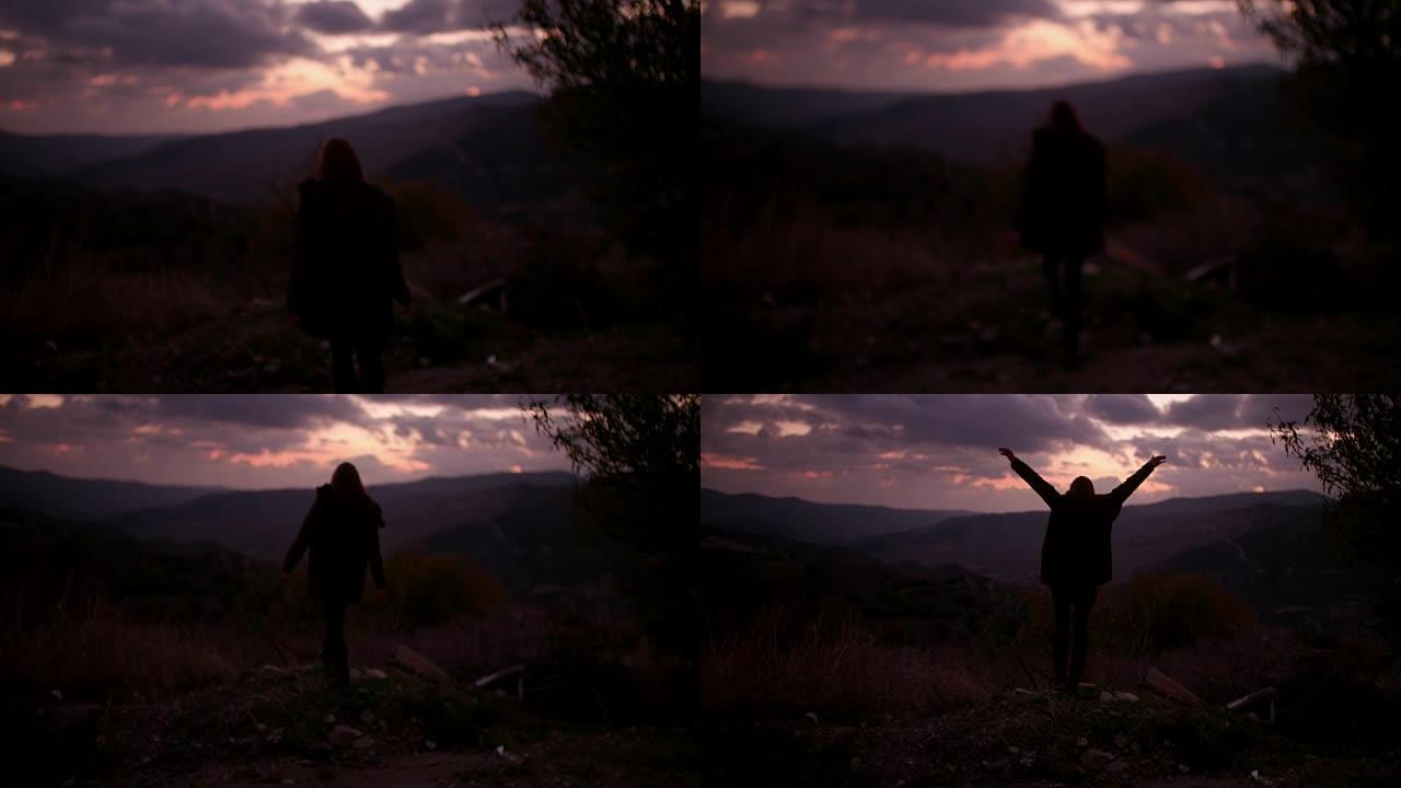女人在黄昏时抬起手臂在山顶上