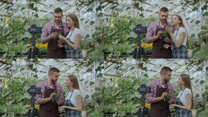 年轻微笑的博主夫妇园丁围着围裙，拿着花说话，录制在线园艺视频博客