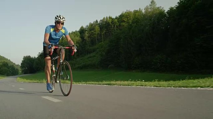 低角度: 在大自然中训练的男性公路自行车手赶上并超越了相机。