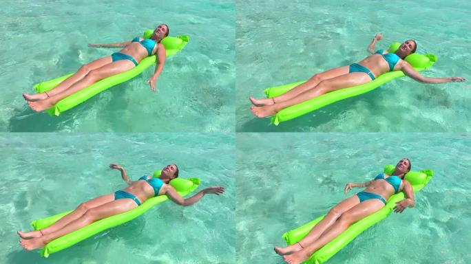慢镜头特写:微笑的女人在比基尼躺和日光浴在空气床筏漂浮在碧绿的海洋水面在太平洋岛屿天堂
