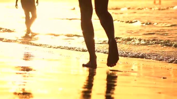 慢动作特写: 人们在惊人的金色日落中沿着海滩散步