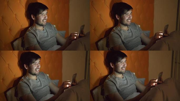 年轻的微笑男子使用智能手机冲浪社交媒体晚上躺在家里的床上