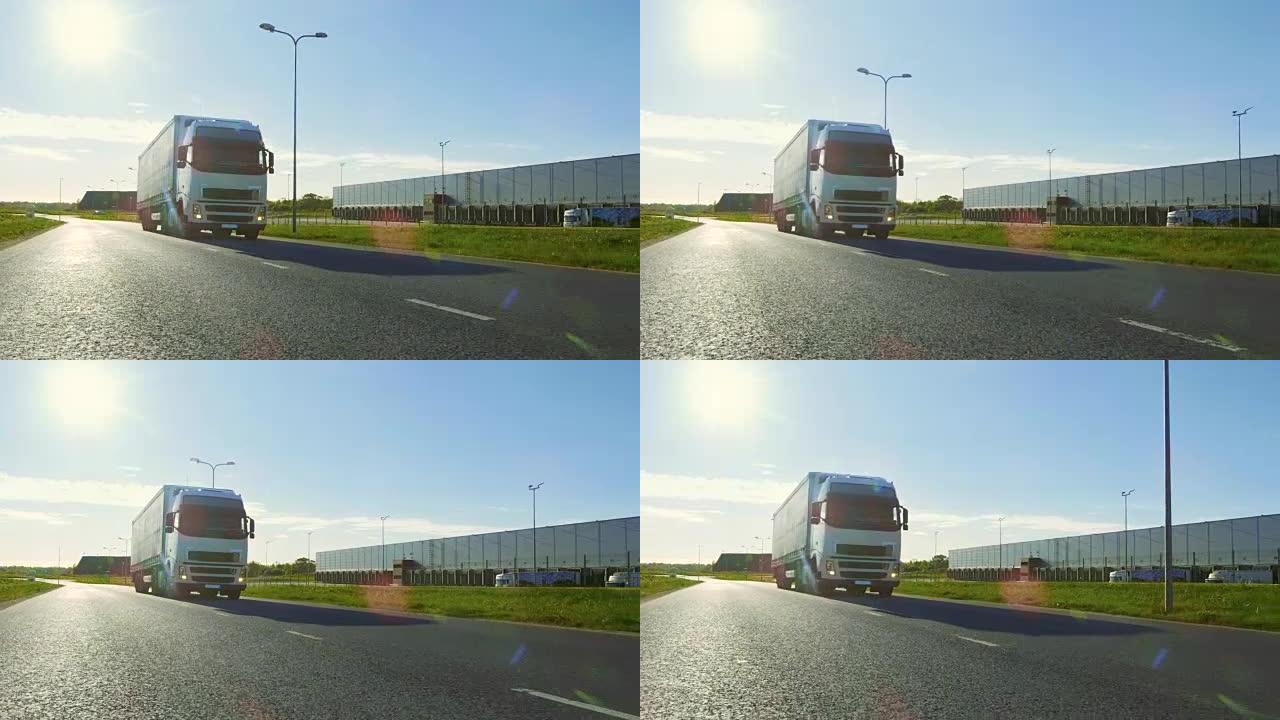 带有货运拖车的白色半卡车在工业仓库区域的空旷道路上移动，背景是阳光普照。