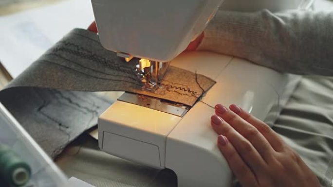 现代电动缝纫机缝制织物的特写视图。女孩修剪整齐的手和五颜六色的缝纫线可见。
