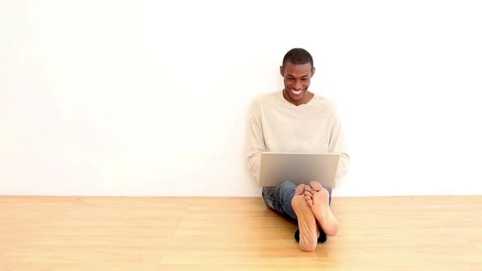 微笑的男人坐在地板上使用笔记本电脑