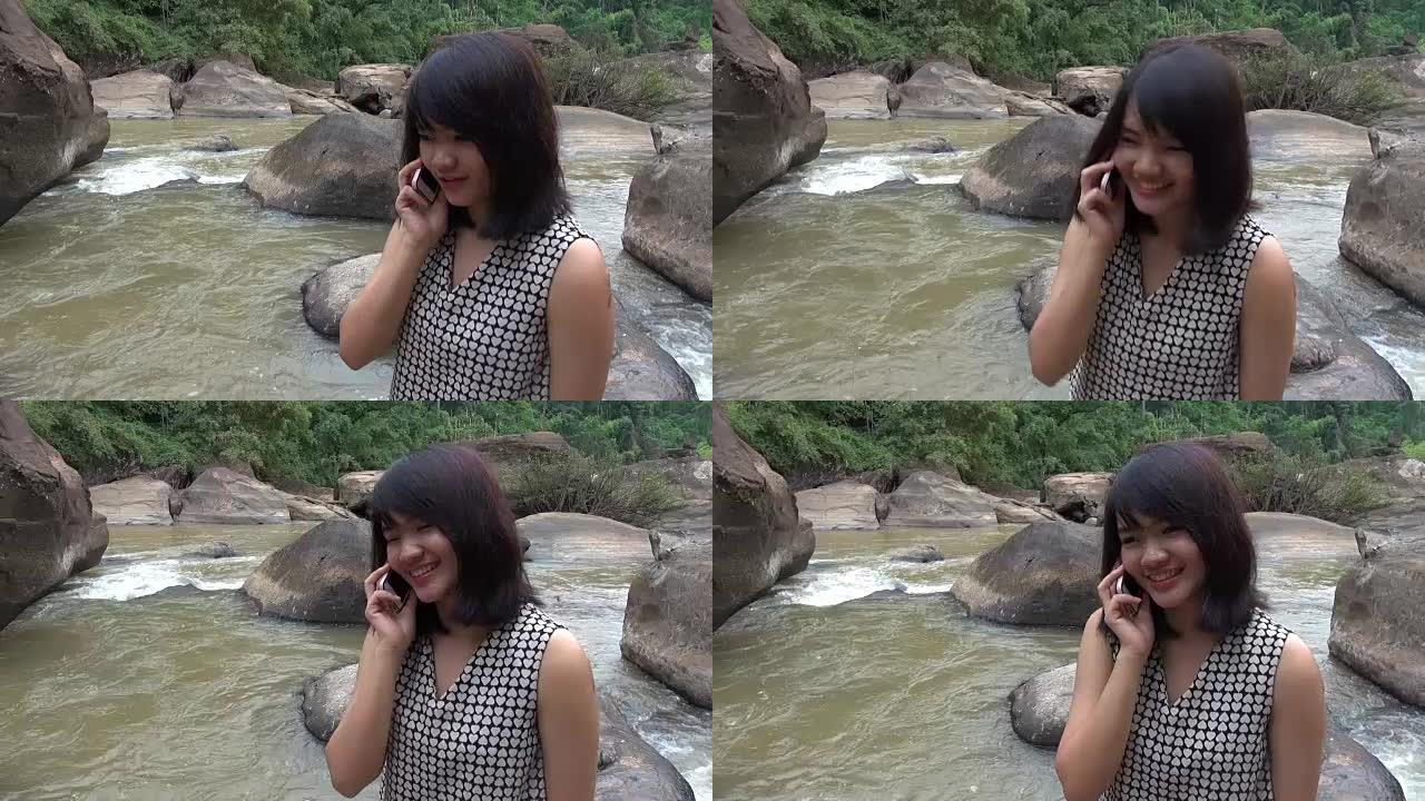 迷人的女人在美丽的瀑布旁用手机聊天