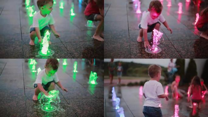 可爱的小男孩在炎热的夏日里在喷泉里玩彩色的喷水器，跑向一群孩子