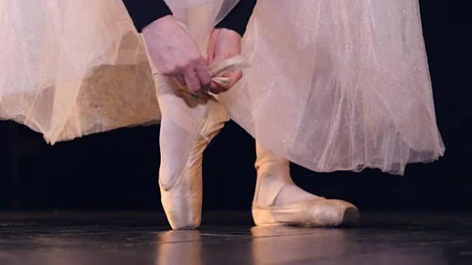 芭蕾舞女演员将芭蕾舞鞋的鞋带绑在脚踝上。