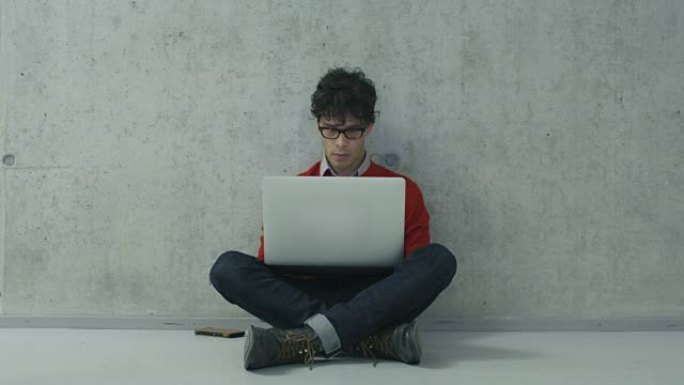 西班牙裔男学生坐在大学走廊上，正在笔记本电脑上工作。